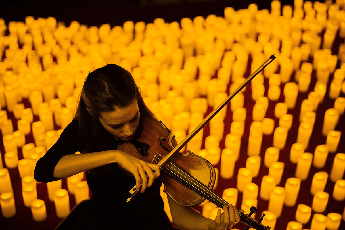 woman playing the violin in front of a floor full of candles