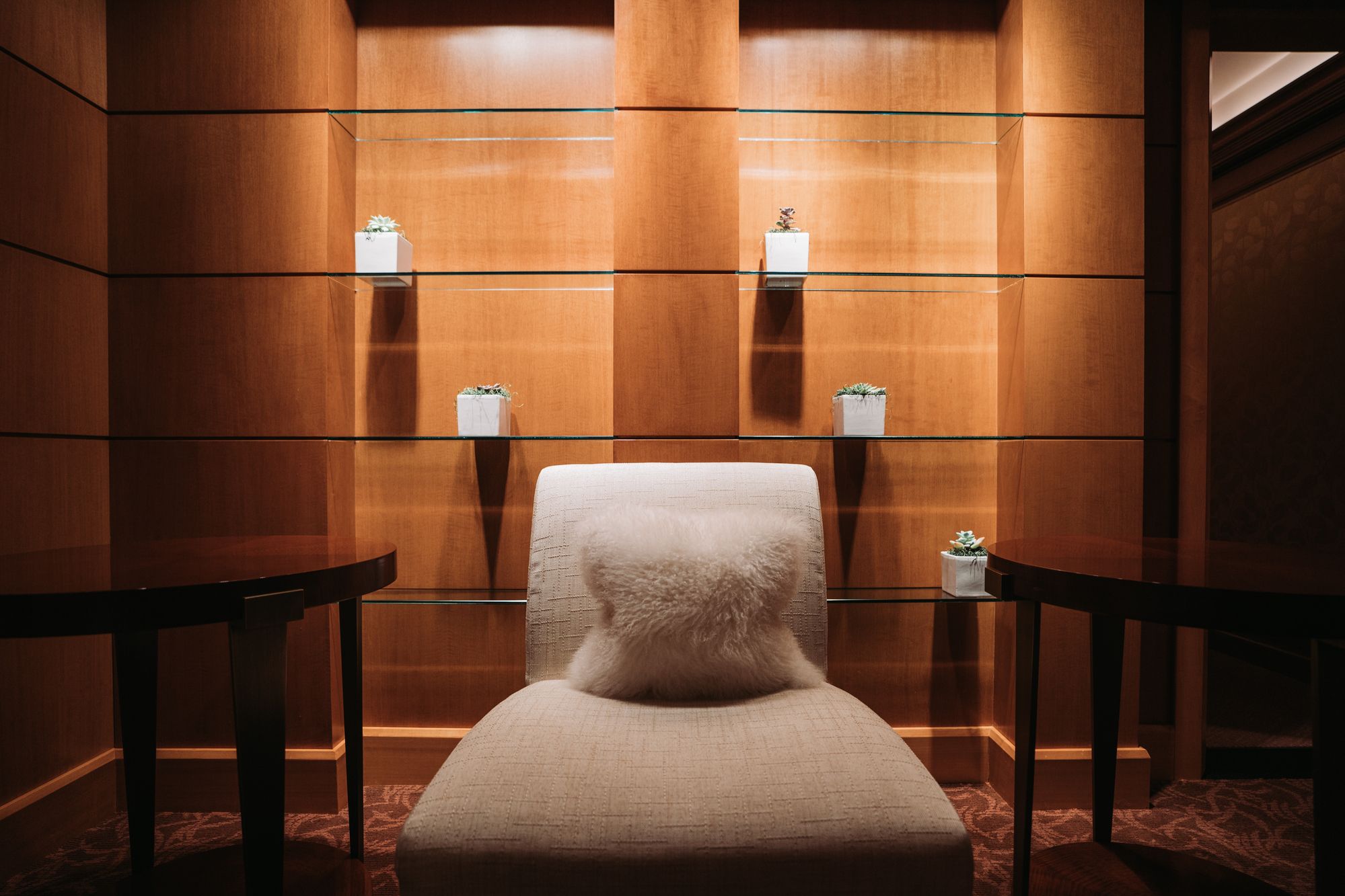 Grand Spa relaxation lounge with a cream chaise lounge, warm wood paneling, and glass shelves with succulent arrangements at The Grand America Hotel.