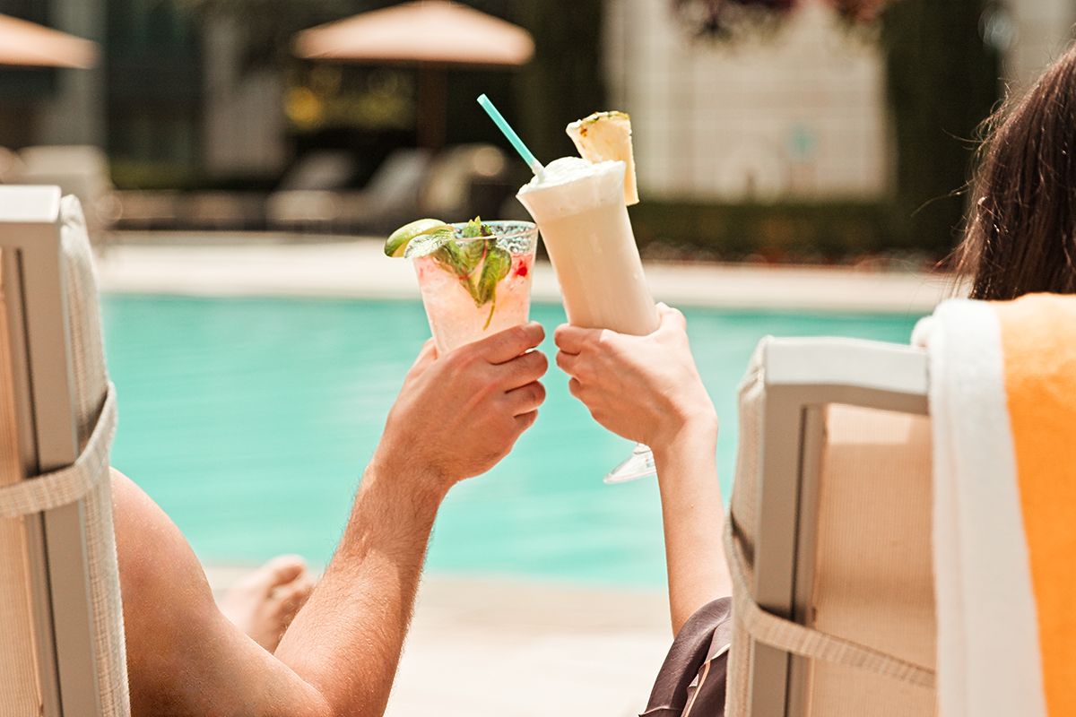 A couple cheersing their drinks next to the pool