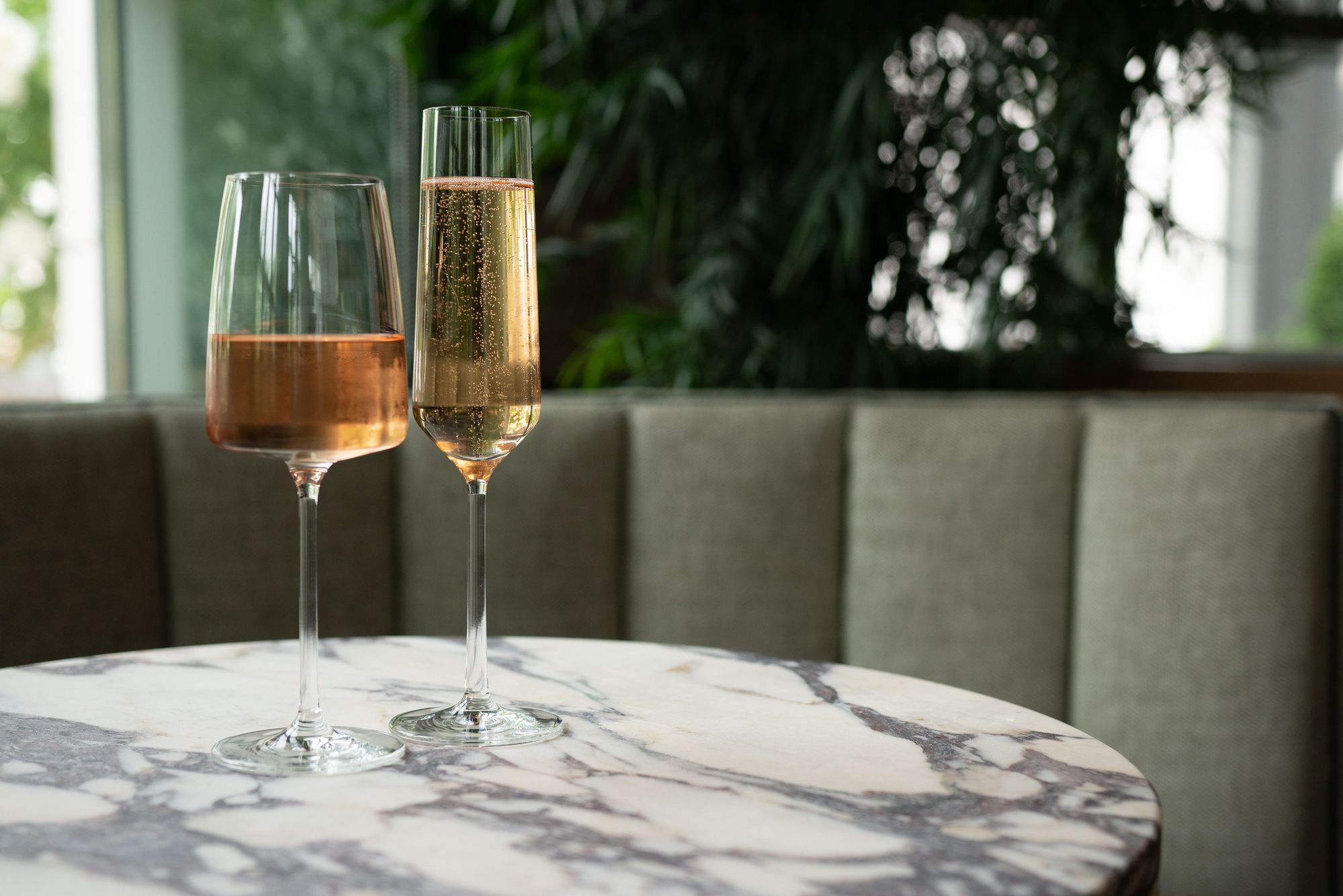 A glass of rose wine and a glass of champagne sit atop a marble-top table at a booth at Laurel Brasserie and Bar.