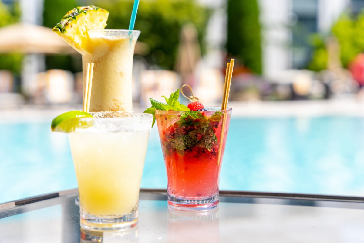 three different types of drinks on a table next to the pool
