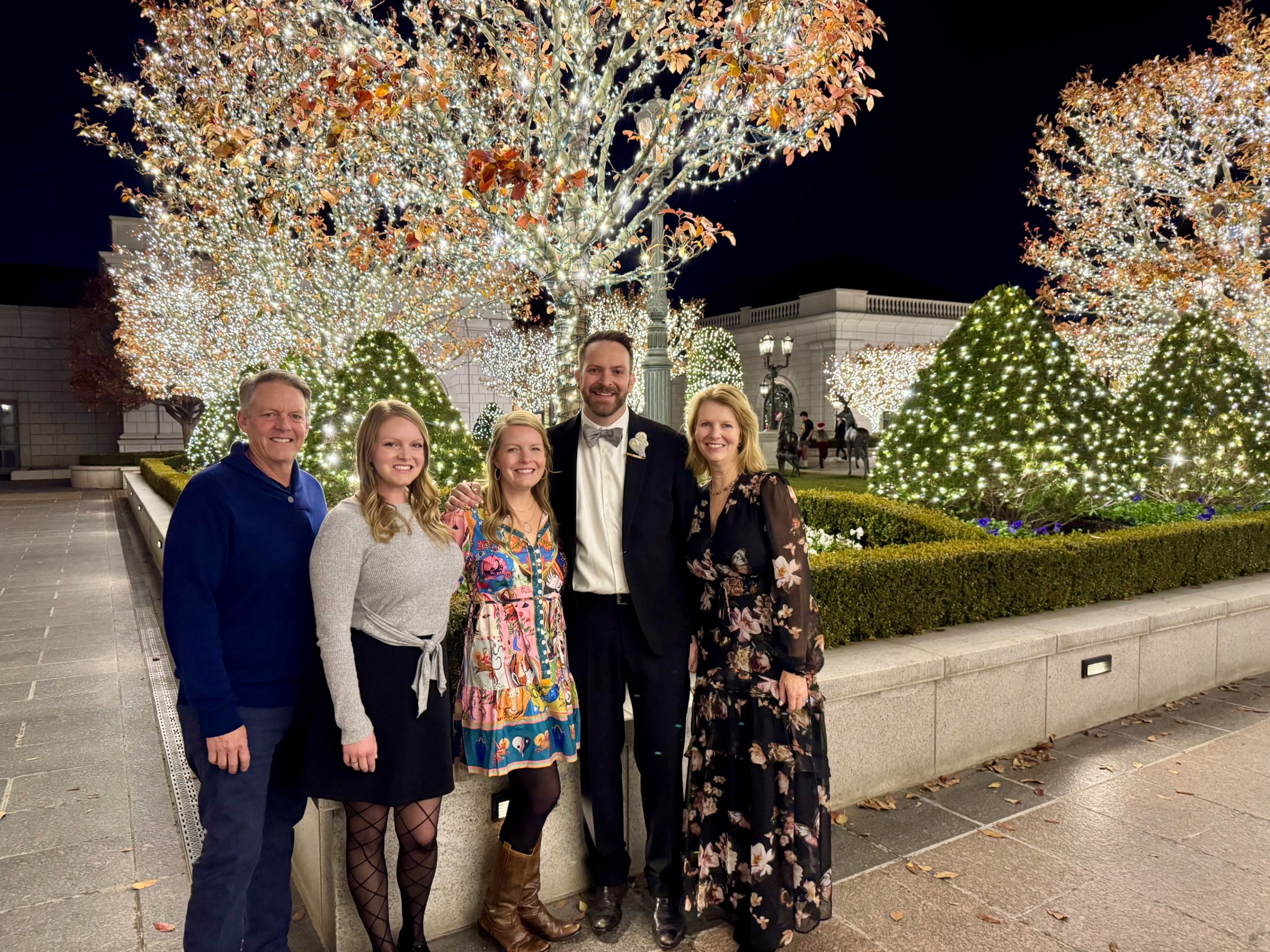 Family posing for photo in Grand courtyard at night with trees lit up with holiday light