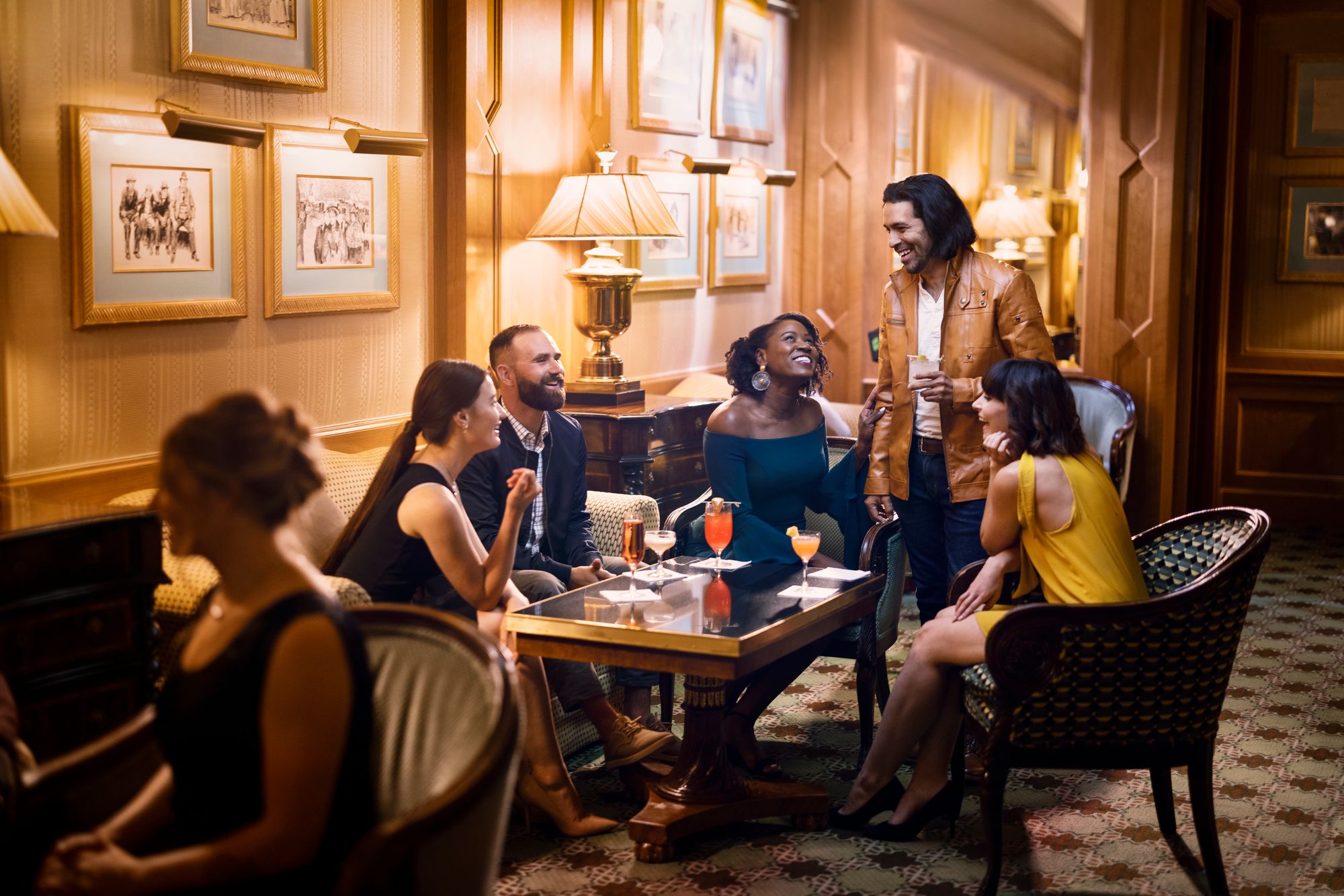 A group gathers joyfully in the Gibson Lounge, sharing drinks and smiles.