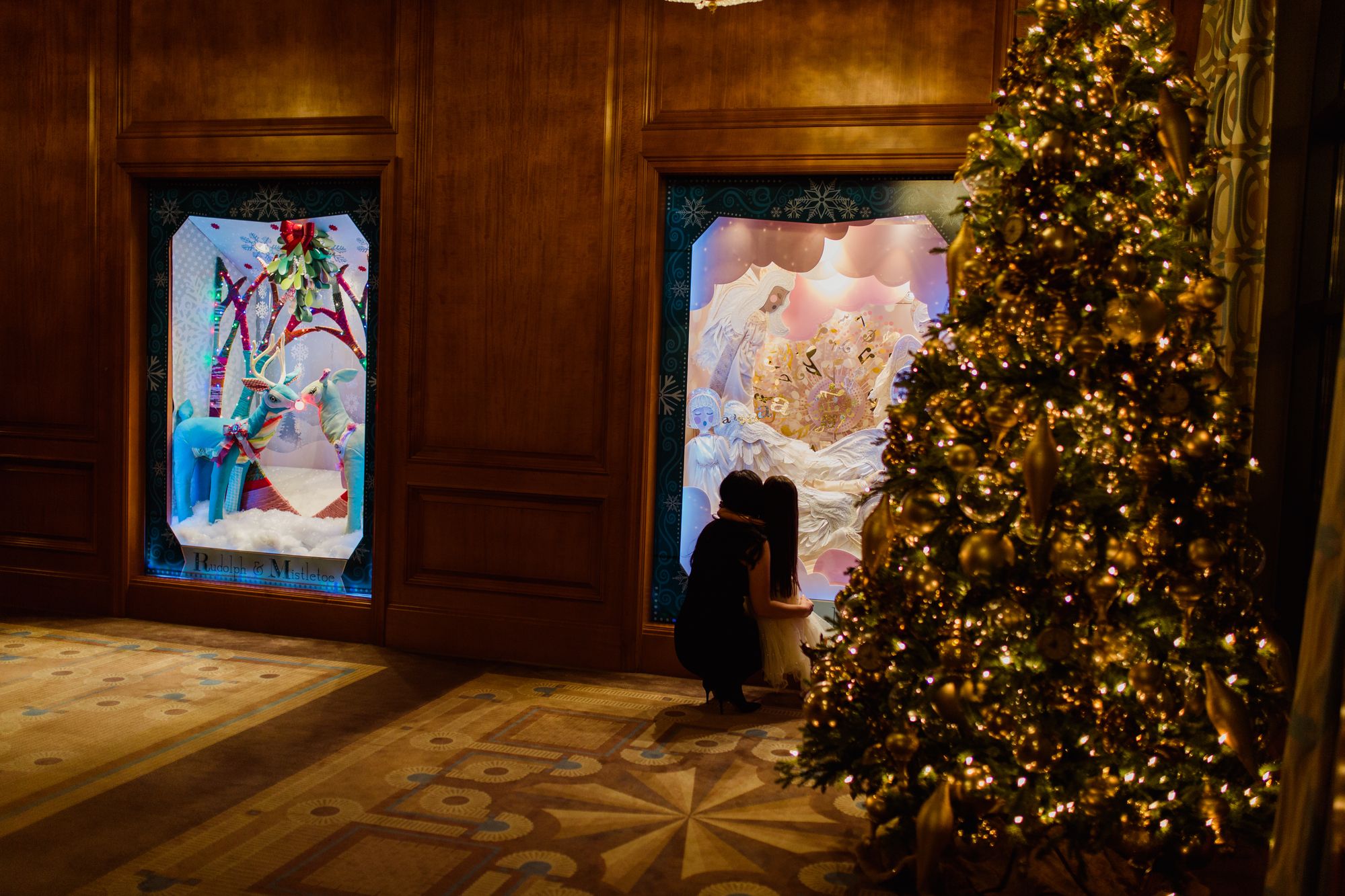 parent and child hugging while looking at holiday window displays