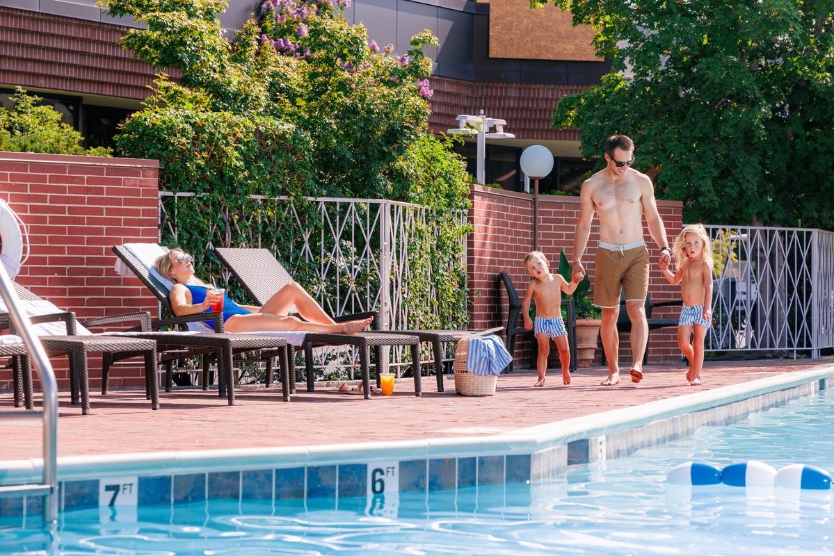 a woman laying in lounge chair next to the outdoor pool at Little America Hotel in Salt Lake City as her husband and children walk to her