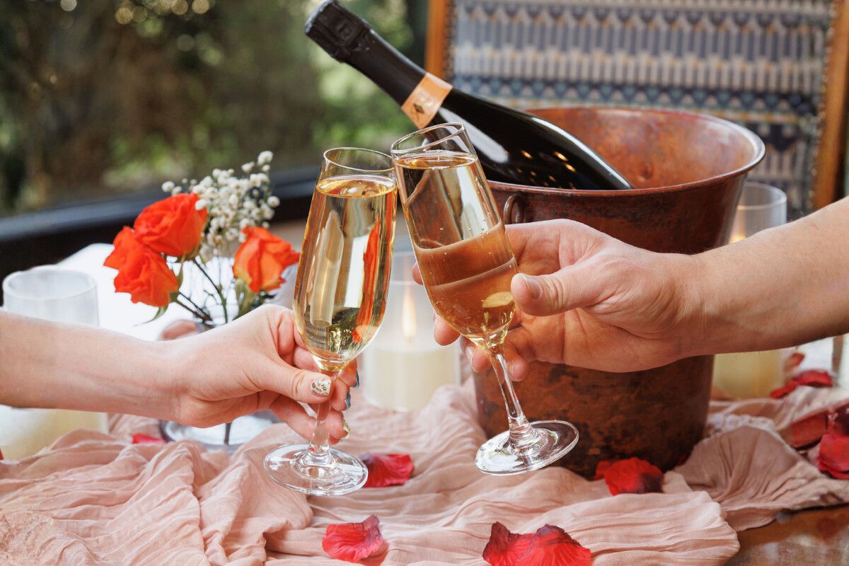 Two glasses of champagne with a bottle in a chiller with rose petals on the table